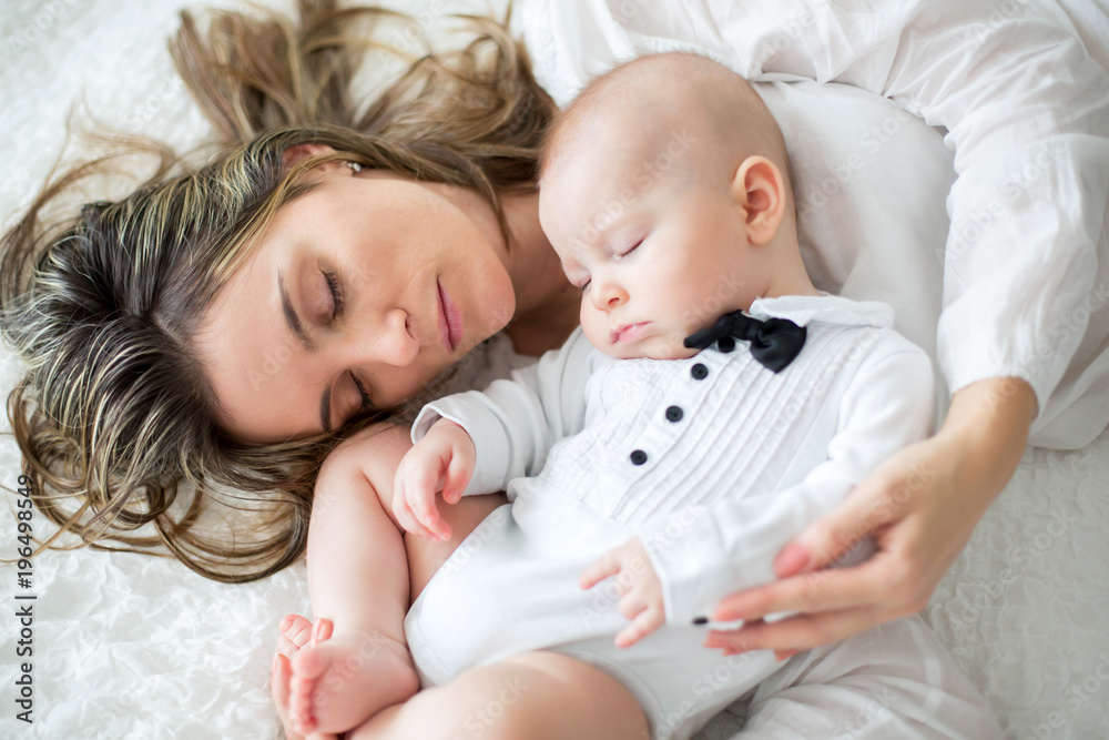 Mother and her baby son, sleeping on a big bed, soft back light