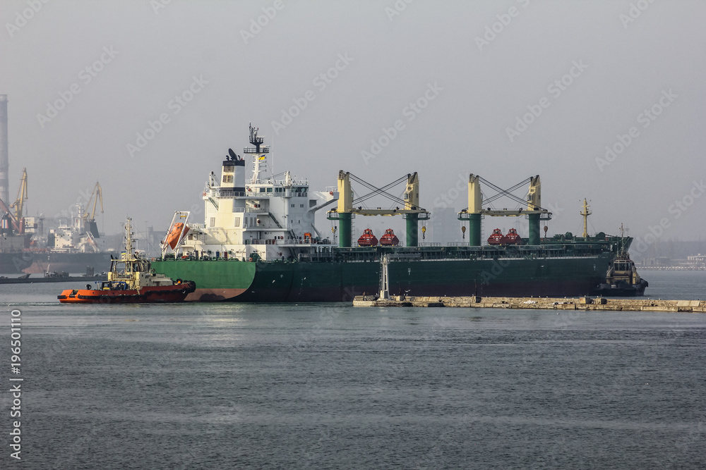 Back view. Tugboat towing a large cargo ship in port. Odessa sea port of Ukraine