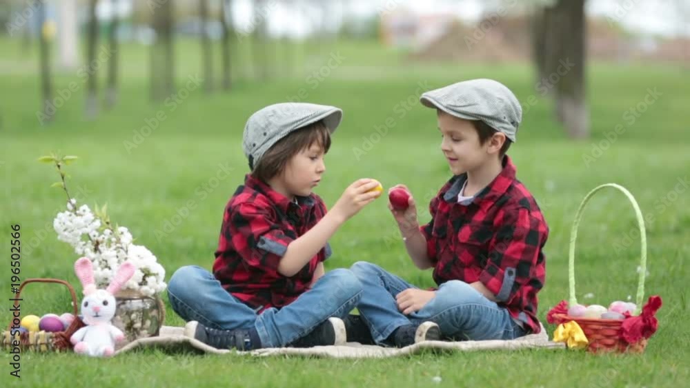 Two children, boy brothers, having fun with easter eggs in the park, beautiful spring blooming garden Two children, boy brothers, having fun with easter eggs in the park, beautiful spring blooming garden