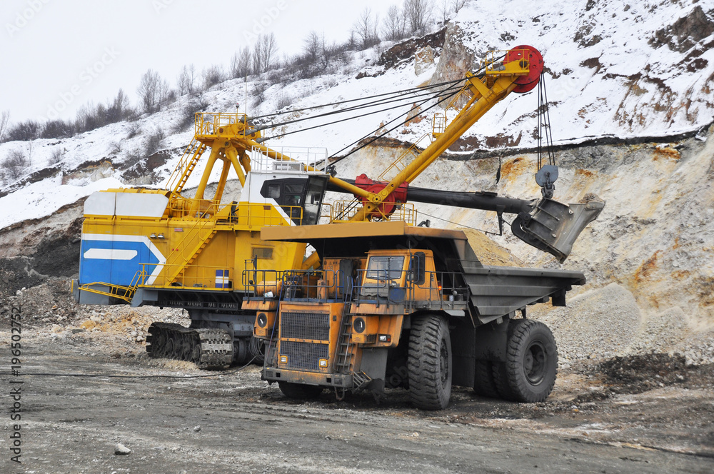 Excavator loads dump truck in quarry in winter
