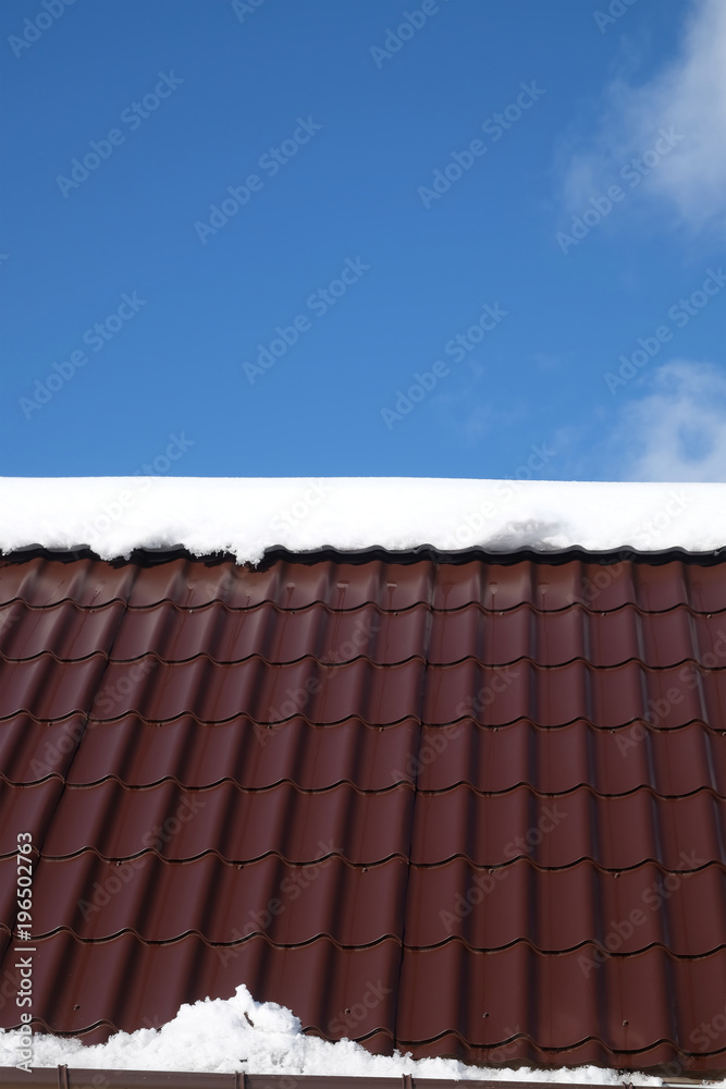Naklejka premium Side of country house roof from brown metal tile with snow in sunny spring day under blue sky with white clouds vertical front view