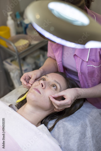 The cosmetologist - professional examines the skin of the patient s face in the office.
