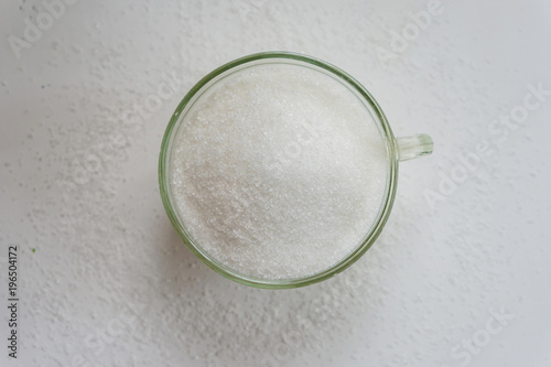 Close up of a glass of white sugar, a white wooden rustic table, shallow depth of focus.