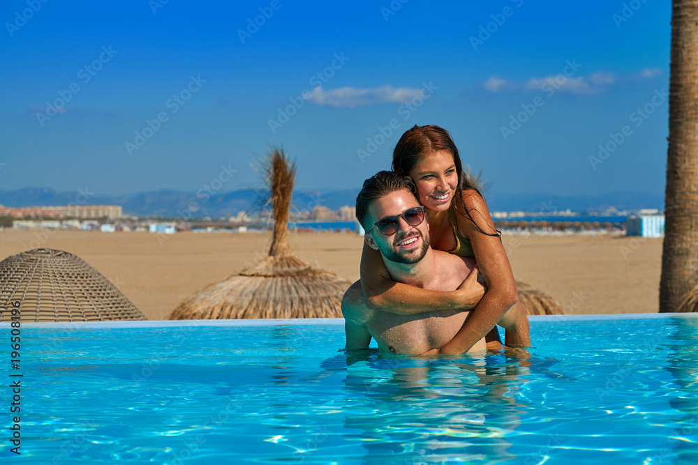 Tourist couple piggyback in infinity pool