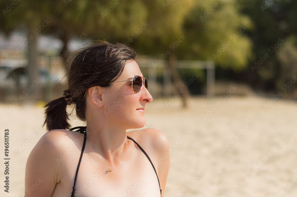 Profile of beautiful young happy Caucasian woman with sunglasses enjoying the sun at the beach