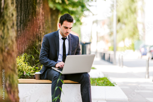 Young businessman use laptop while siiting on the bench at the avenue