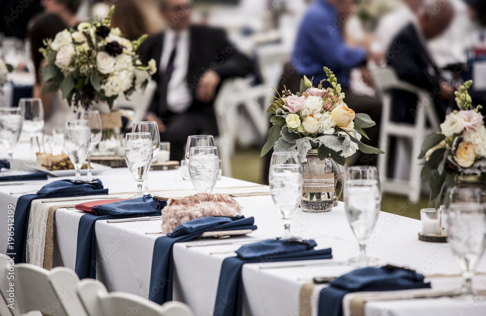 Table set up for wedding reception with people out of focus in background. - obrazy, fototapety, plakaty 