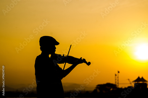 Silhouette boy playing violin with sun set.