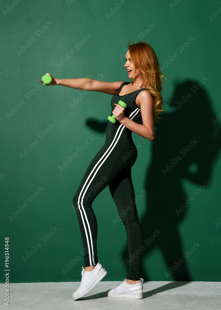 Woman workout exercising with dumbbells in gym on green mint wall background with sunlight. Weight loss concept Woman workout exercising with dumbbells in gym on green mint wall background with sunlight. Weight loss concept