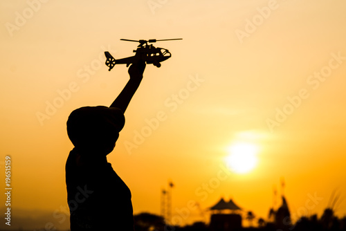 Silhouette boy playing helicopter model with sun set.