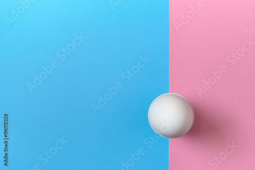 White egg standing on egg cup on blue and pink pastel background, copy space. Boiled egg in stand on paper background with two tone color. Healthy food concept. Easter egg. Flat lay, top view