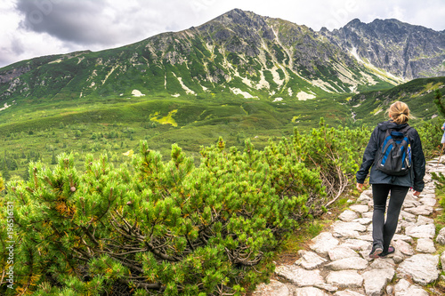 Woman hiking on mountain trail, hiker with backpack on path in high mountains, landscape