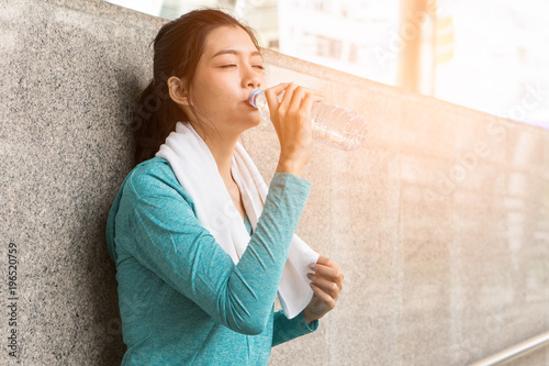 Asian woman drinking water to rehydrate to avoid heat stroke after running outdoors in the summer.