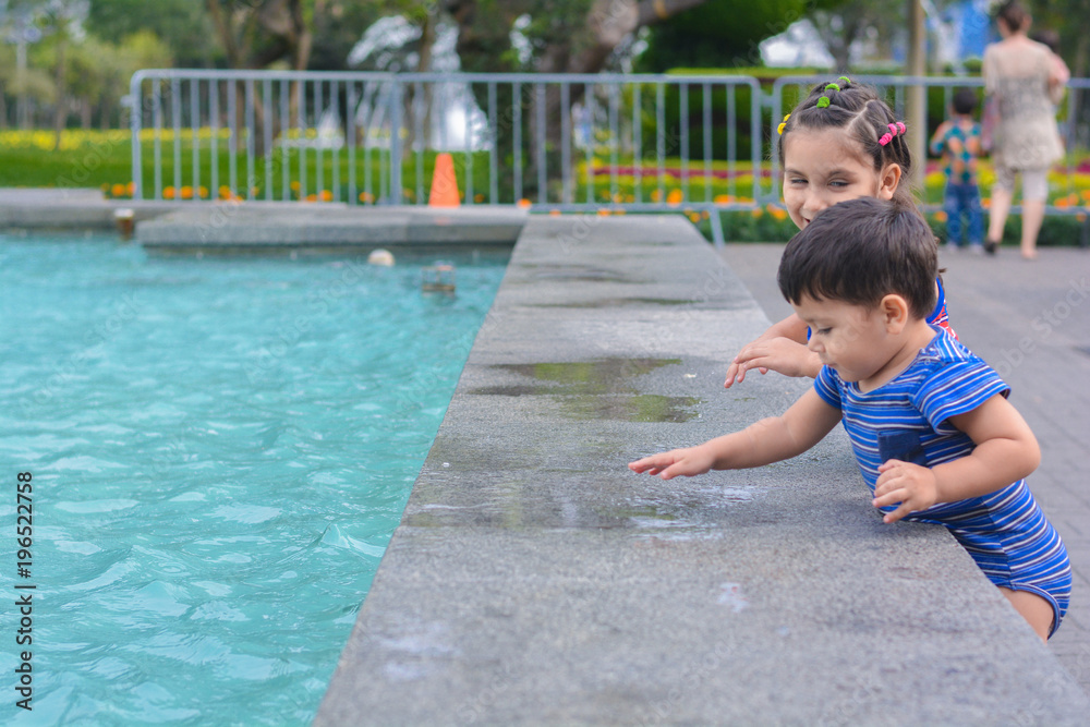 Naklejka premium Little latin sibling playing near to waterpool. 