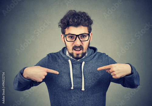 Foto Young angry man in eyeglasses overreacting while pointing at himself looking offended