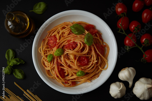 spaghetti dish with tomato sauce and basil on black background