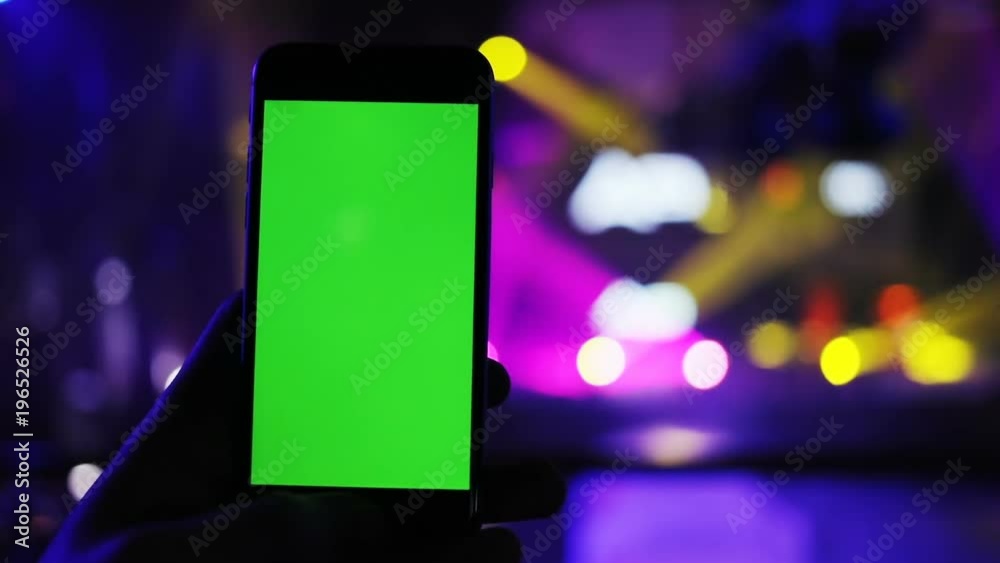 close-up view of modern digital smartphone and colorful concert lighting on background / green screen chroma key mockup content light night club party streaming online app web page photo video camera