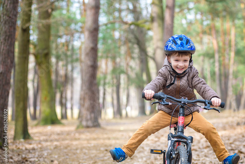 Fototapeta Naklejka Na Ścianę i Meble -  Happy kid boy of 3 or 5 years having fun in autumn forest with a bicycle on beautiful fall day. Active child wearing bike helmet. Safety, sports, leisure with kids concept.