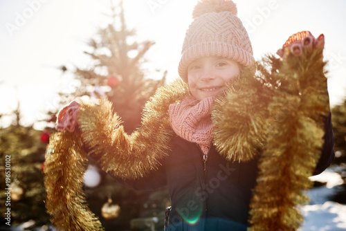 Girl in christmas tree forest wearing tinsel, portrait photo