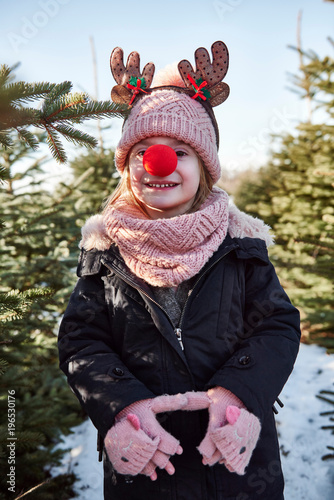 Girl in christmas tree forest with red nose, portrait photo