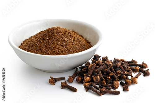 Ground cloves in white ceramic bowl isolated on white. Whole cloves. photo