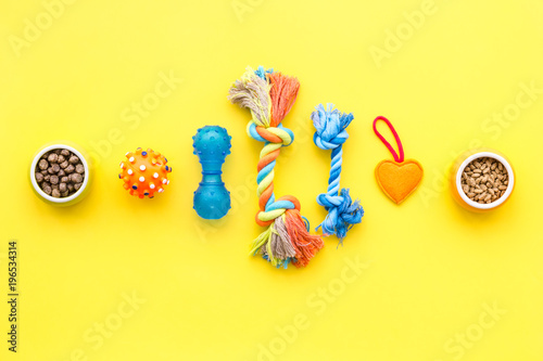 toys for pets and dry food on yellow background top view space for text