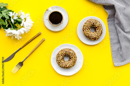 modern breakfast desing with sweet donut, coffee and flowers on woman yellow desk background top view photo