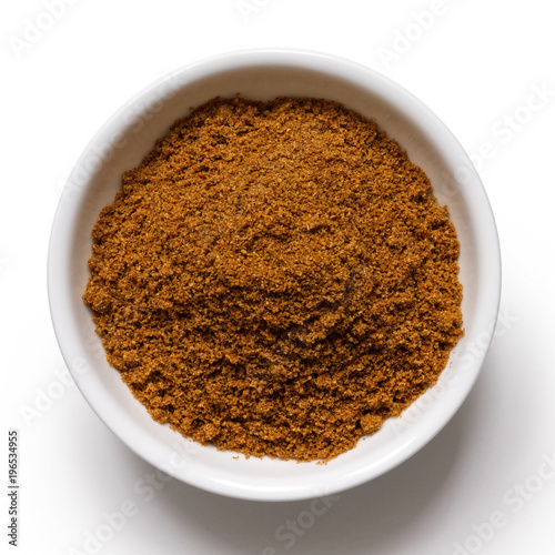 Ground cumin in white ceramic bowl isolated on white from above.