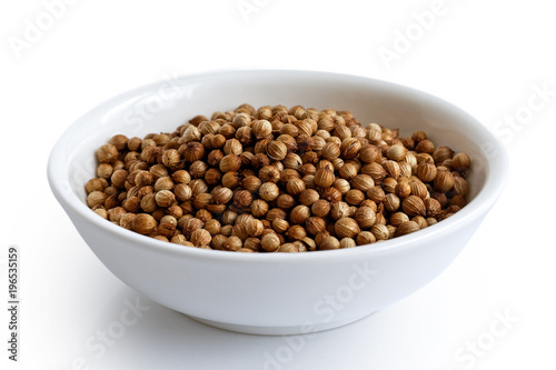 Whole dried coriander seeds in white ceramic bowl isolated on white.