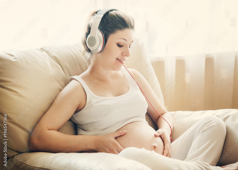 Portrait of pregnant woman sitting on sofa at home and listening music in headphones. Portrait of pregnant woman sitting on sofa at home and listening music in headphones.