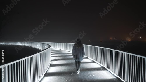 Woman walking at night on an illuminated bridge
