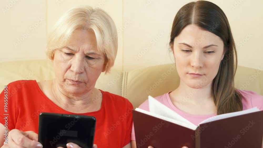 Mother reading ebook and daughter reading physical print book. Concept