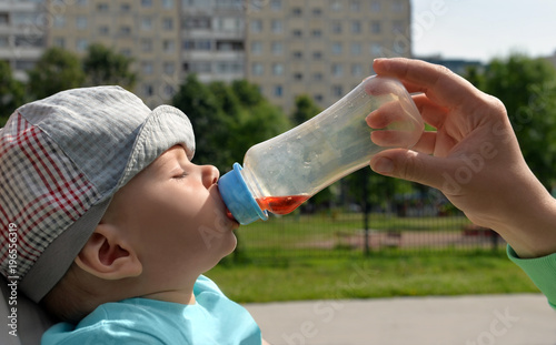 Head of  falling asleep baby and hand of his mother who gives  drink to him. photo