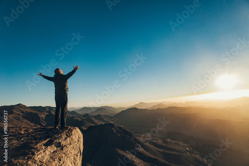 Man stands facing rising sun with lift up his arms on Mount Sinai.