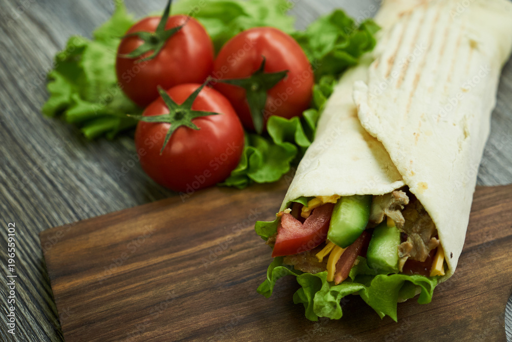 Shaurma sandwich chicken roll in a pita with fresh vegetables tomatoes , cucumber, latitude, cheese and chicken breast meat on wooden cutting board Shaurma sandwich chicken roll in a pita with fresh vegetables tomatoes , cucumber, latitude, cheese and chicken breast meat on wooden cutting board