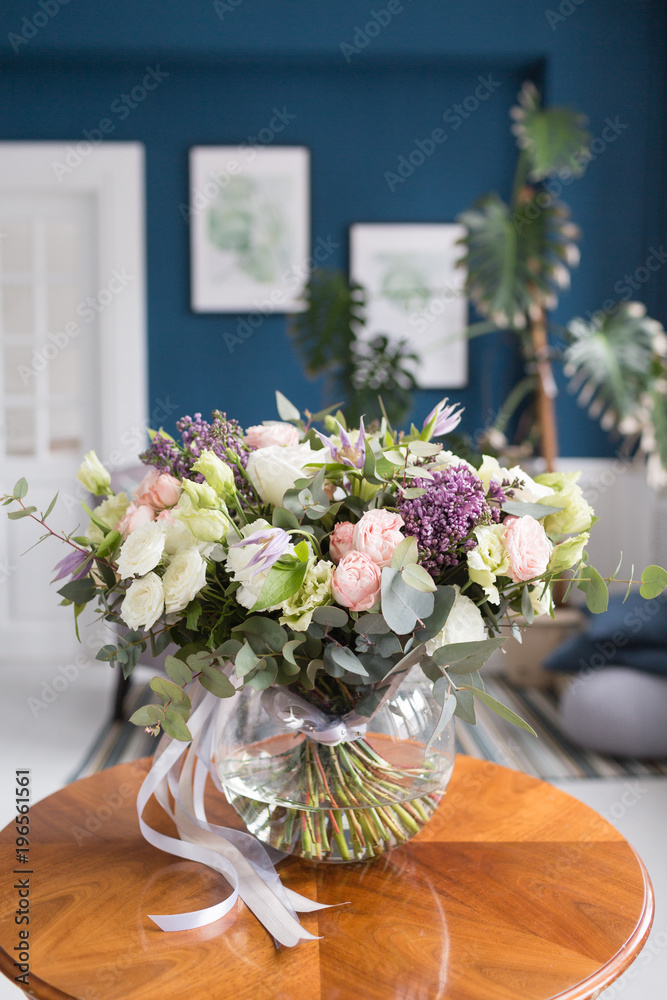 Sunny spring morning in living room. Beautiful luxury bouquet of mixed flowers in glass vase on wooden table. the work of the proffesional florist at a flower shop. Sunny spring morning in living room. Beautiful luxury bouquet of mixed flowers in glass vase on wooden table. the work of the proffesional florist at a flower shop.