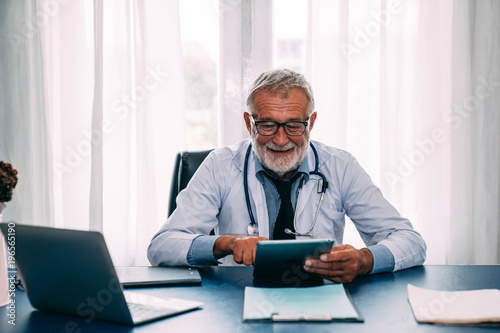 Senior doctor at desk looking at his tablet