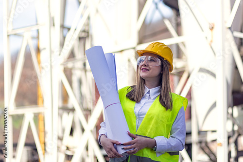 Female engineer wearing helmet and reflective vest holding blueprint