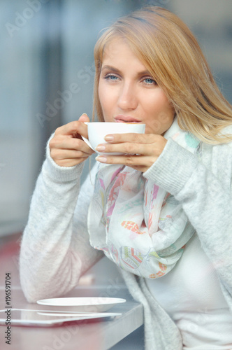 Portrait of a pensive girl drinking coffee and looking outdoors through a window