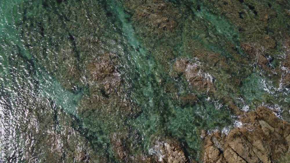 A dynamic drone shot of waves lapping against the rocks in the ocean. 