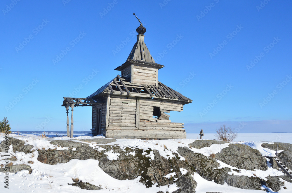 Россия, Ладожское озеро, разрушенная покосившаяся часовня на острове в ясный зимний день Россия, Ладожское озеро, разрушенная покосившаяся часовня на острове в ясный зимний день