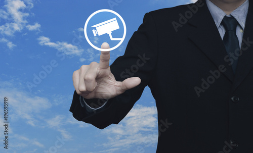 Businessman pressing cctv camera icon over blue sky with white clouds, Business security concept