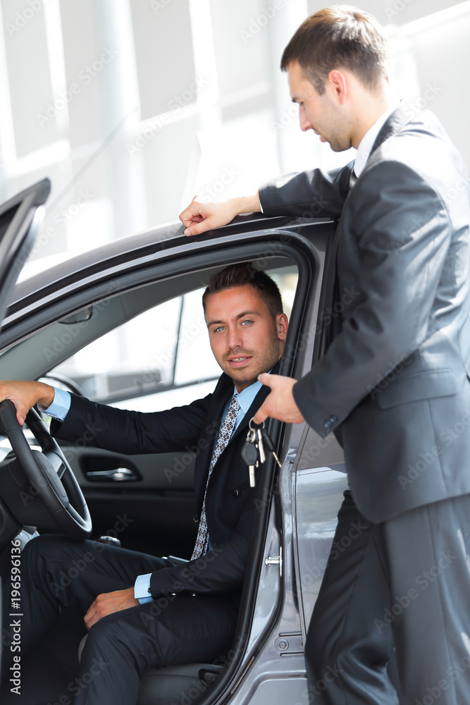 successful businessman, receiving the keys to the car from the seller in the showroom successful businessman, receiving the keys to the car from the seller in the showroom