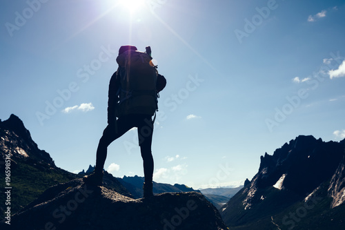 Silhouette of woman with backpack hiking on sunrise mountain top