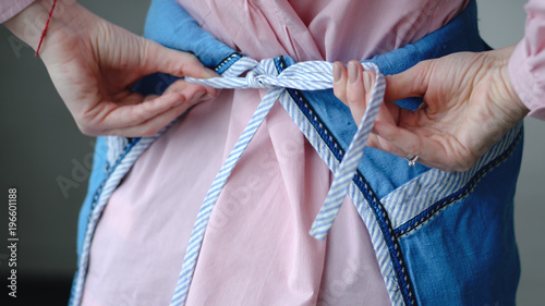 The girl ties up an apron. Hands closeup.