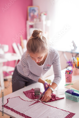 young woman seamstress making pattern on fabric with tailors chalk. Girl working with a sewing pattern. Hobby sewing as a small business concept. Tailor measuring textile material