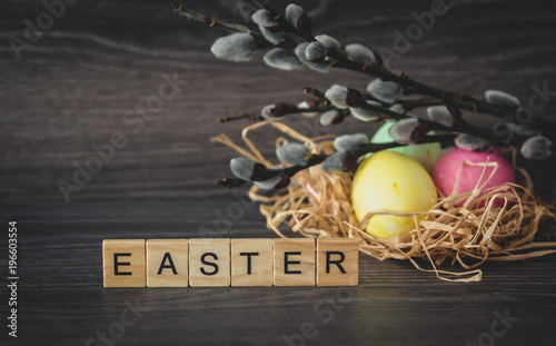 Easter word of light wooden tablets, willow twigs with seals and painted eggs in nest on dark wooden background