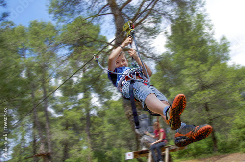 Leisure and activities on nature. Small boy hanging and walking on cables between trees.