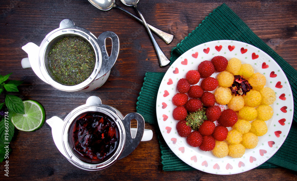 Fresh red fruit and green mint tea and plate full of raspberries with jin jang motive Fresh red fruit and green mint tea and plate full of raspberries with jin jang motive