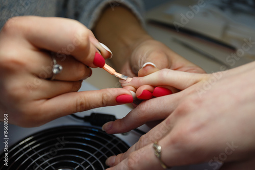 Manicure master, color orange gel nail Polish finger in nail salon. Nails salon woman applying nail Polish on client's hand. Close-up of other manicure tools.
